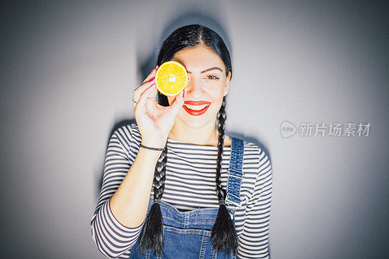 Young Woman holds an Orange in front of her Face